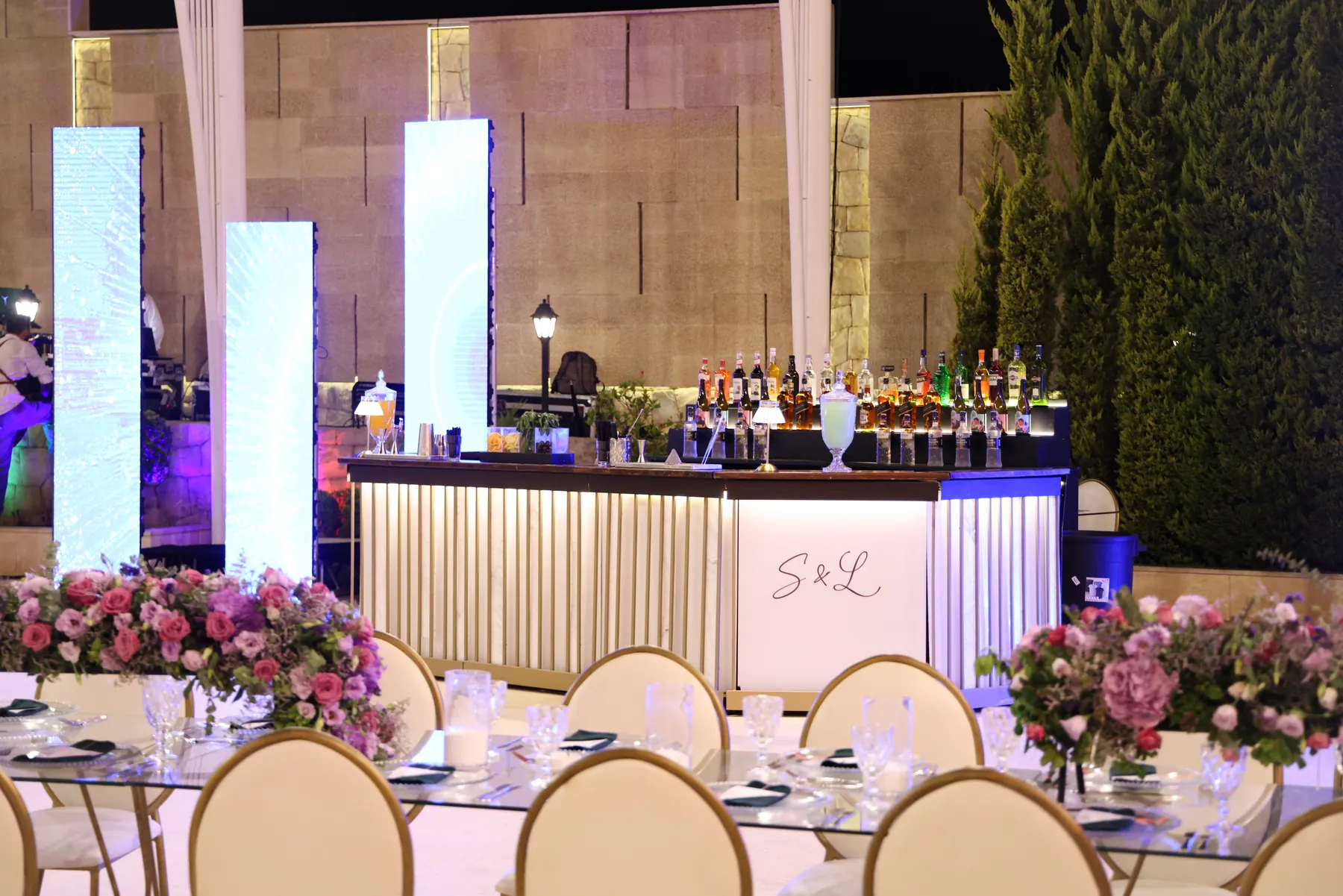 Wide view of the illuminated Pannel Bar behind reception tables and flowers