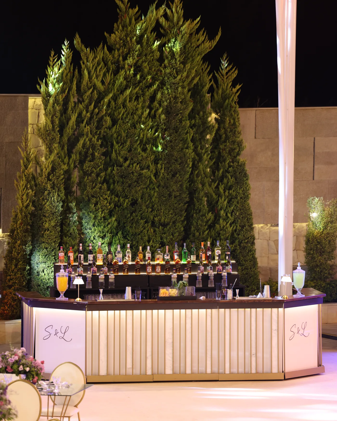 A Malabar bar lit at night against a tall hedge, personalised with the couple's monogram