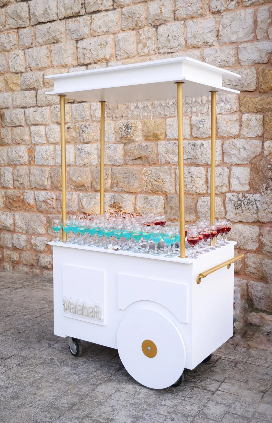 The Cart: a white and gold mobile drinks trolley set with glassware against a stone wall
