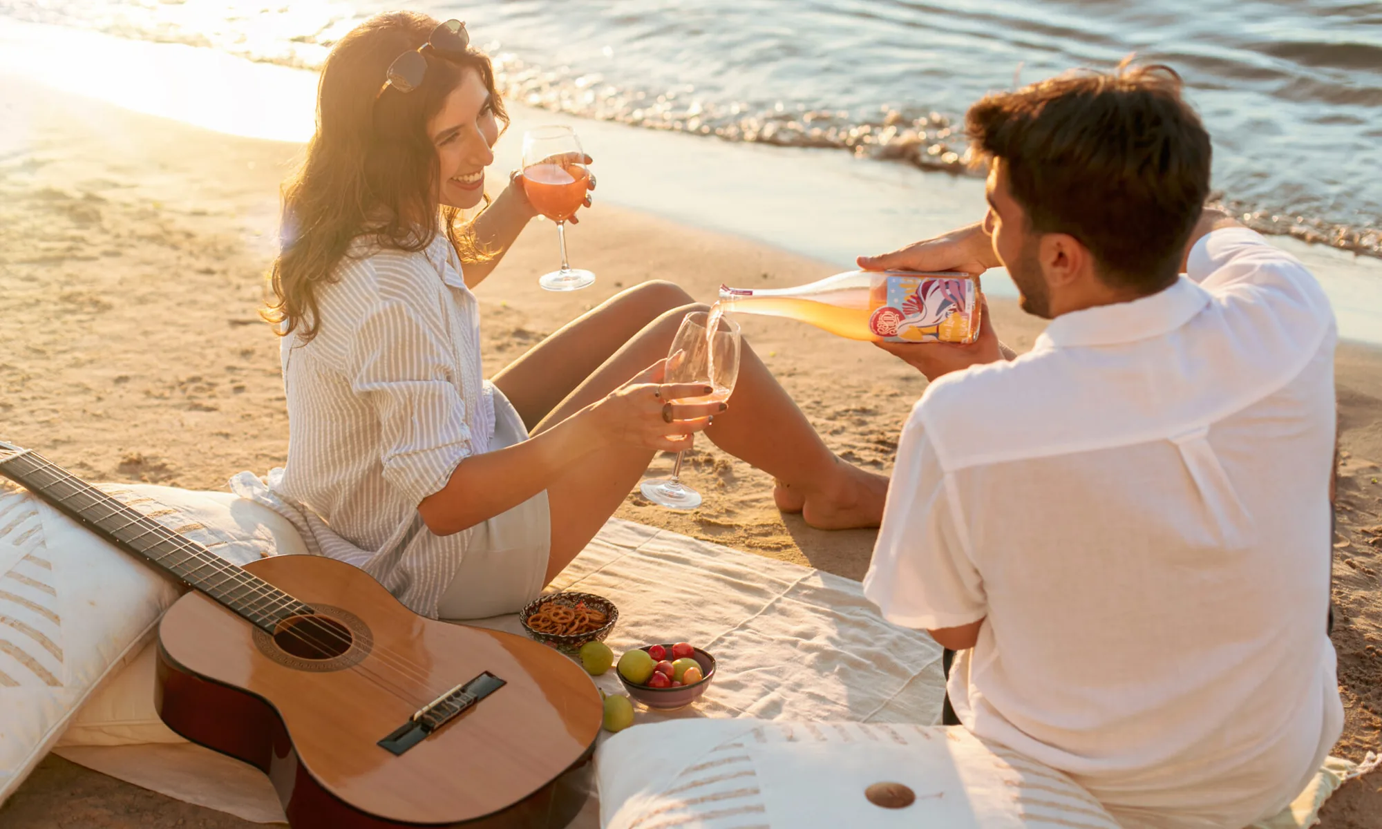Two friends sharing Salud bottled cocktails on the beach at golden hour